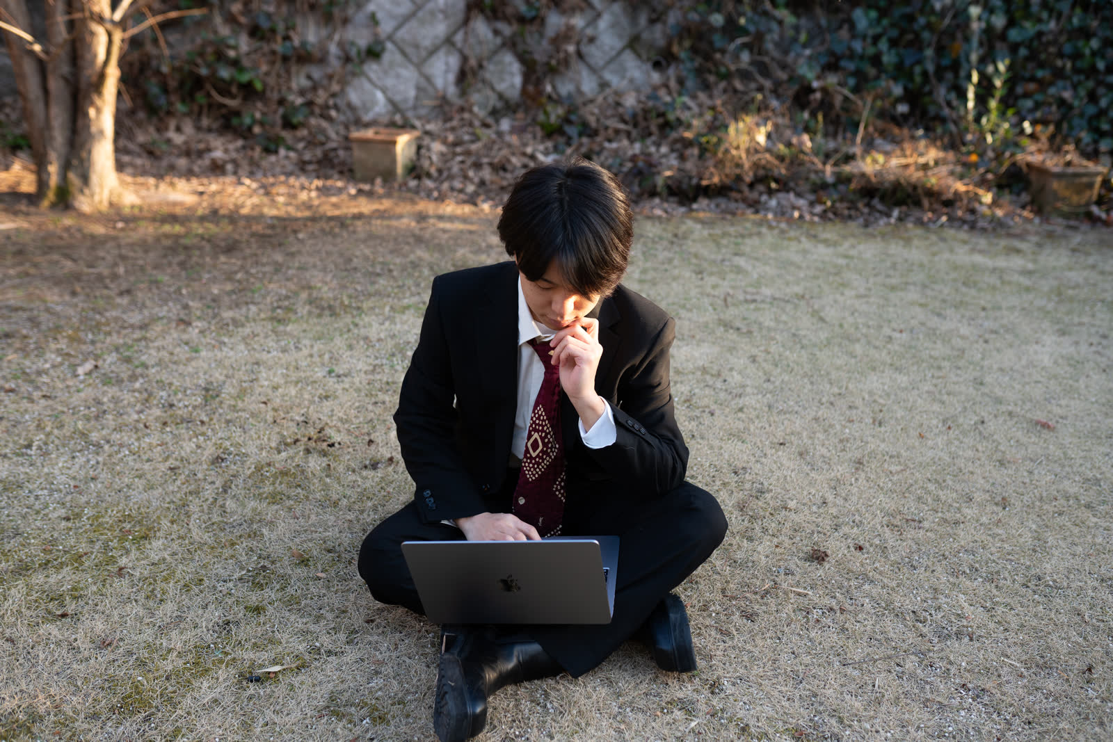 プロフィール写真。屋外でノートPCに向かい、考え込む姿。